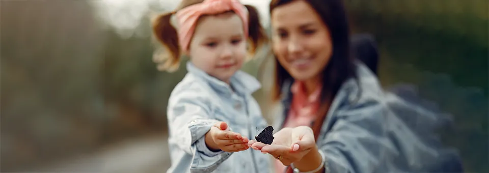 mother and daughter looking at a butterfly in mother's hand 